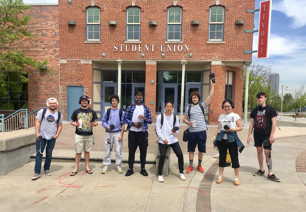 Group of people holding sound recording equipment standing in front of a building that says Student Union on the outside.