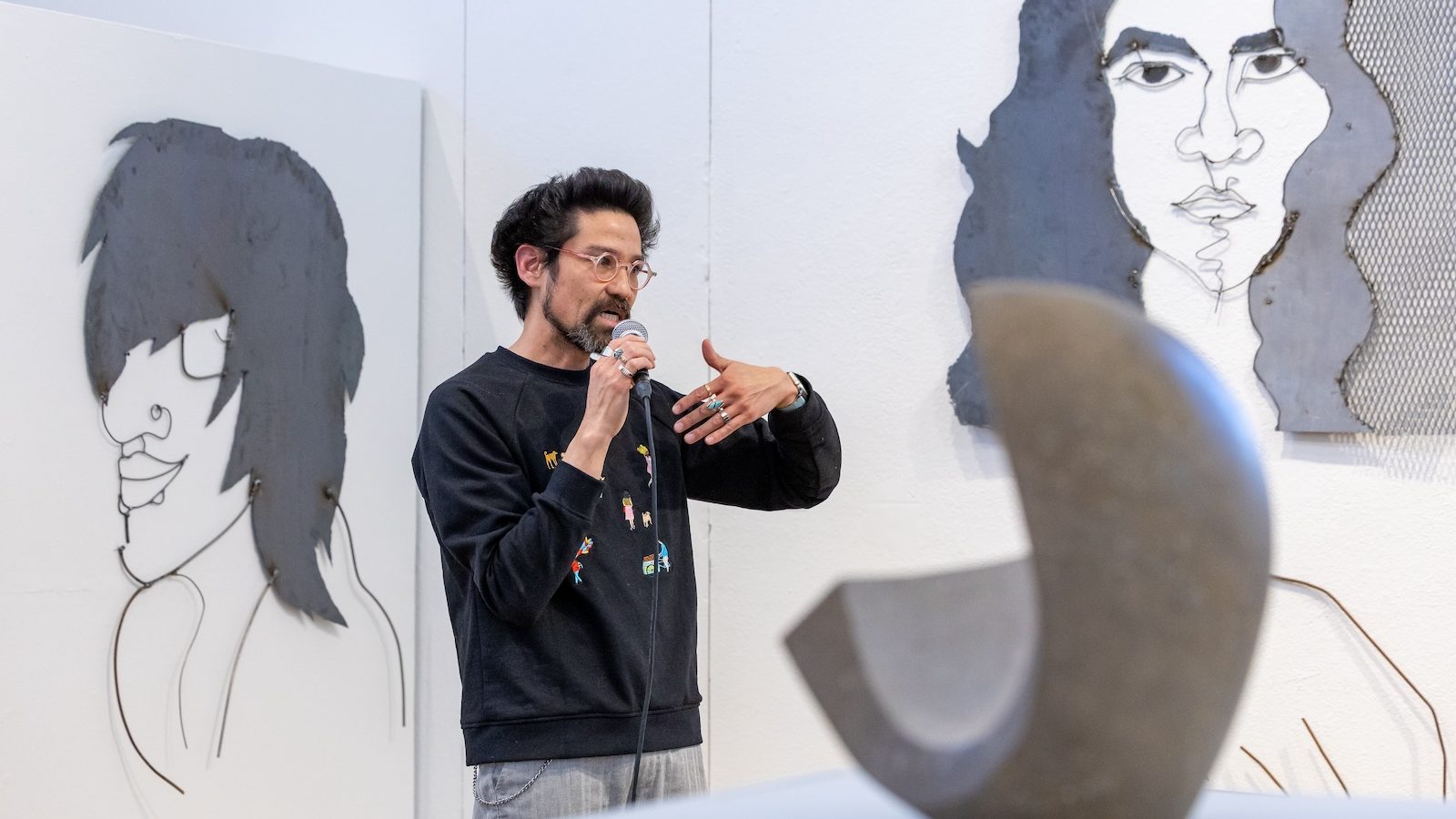 A person speaks using a mic in an art gallery with artwork behind them