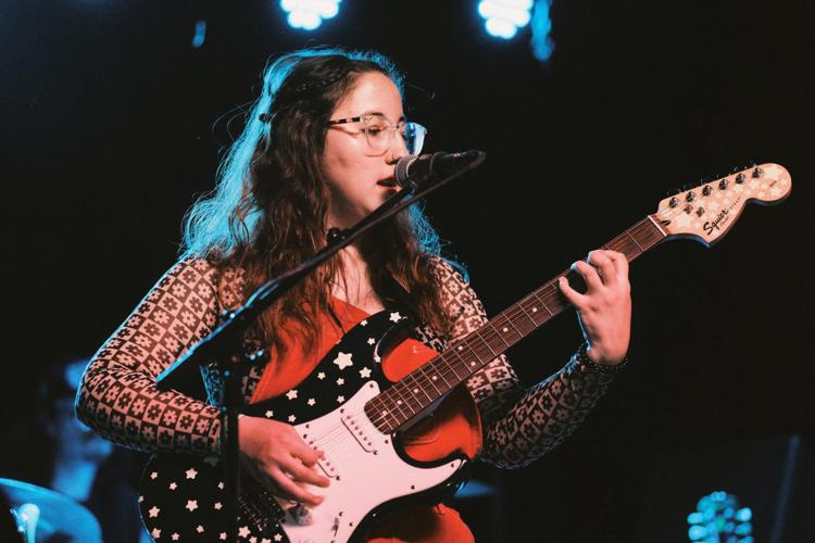 A person plays an electric guitar and sings on a stage